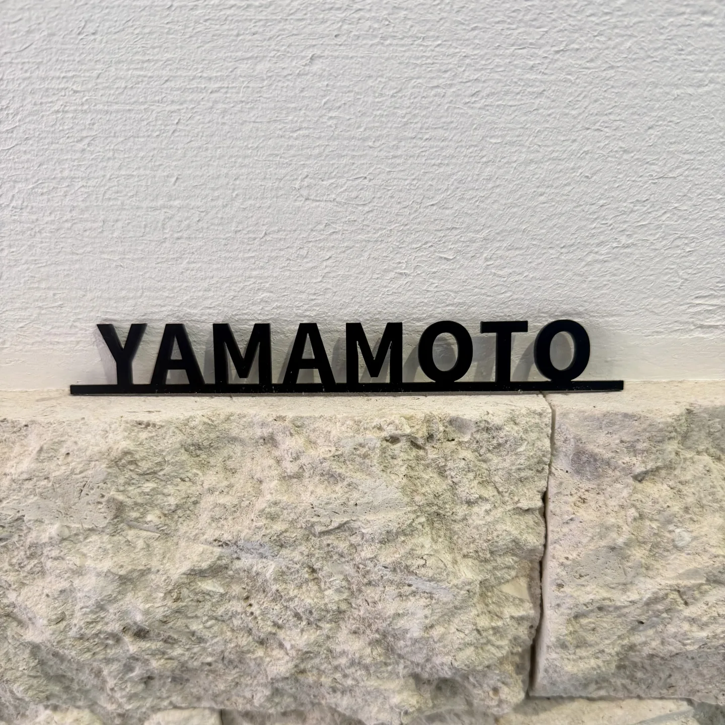 石材を背景に撮影した YAMAMOTO の太字アクリル切り文字表札