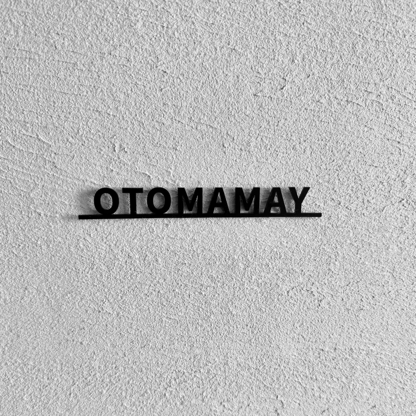 凹凸のある壁面を背景に撮影した OTOMAMAY の太字アクリル切り文字表札