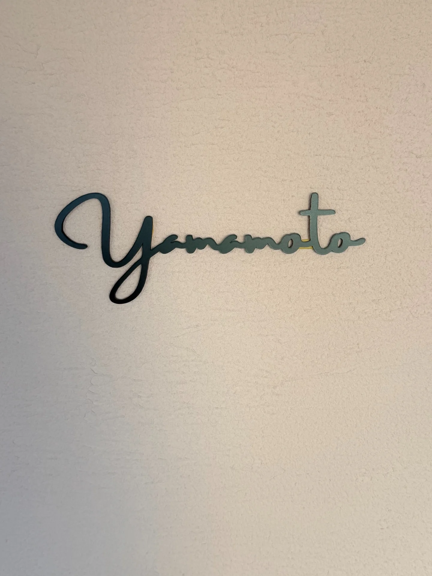 壁面を背景に撮影したマットブラックの筆記体アクリル切り文字表札 Yamamoto